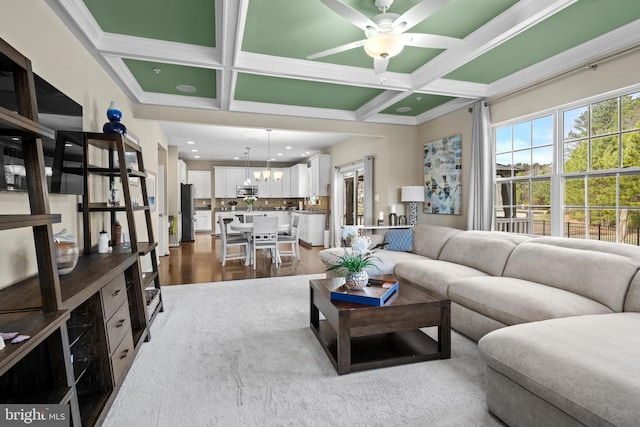 living area with ceiling fan with notable chandelier, coffered ceiling, dark wood finished floors, and beamed ceiling