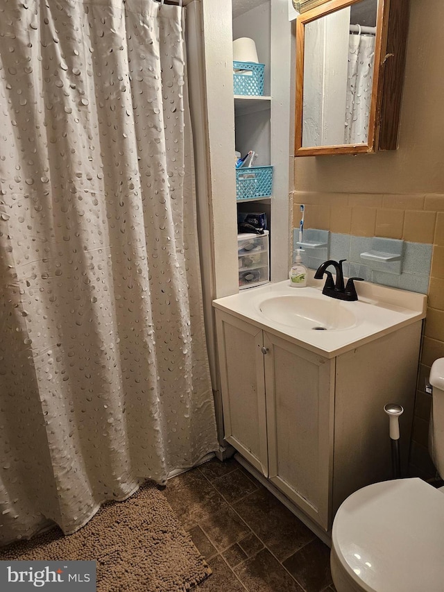 bathroom with toilet, a wainscoted wall, stone finish flooring, vanity, and tile walls