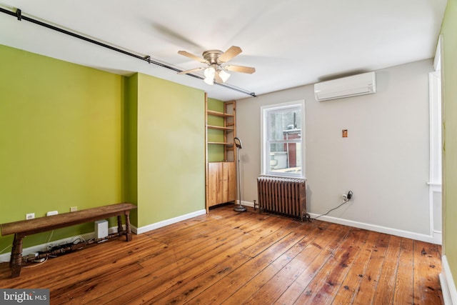 empty room featuring hardwood / wood-style flooring, radiator, a wall mounted AC, and ceiling fan