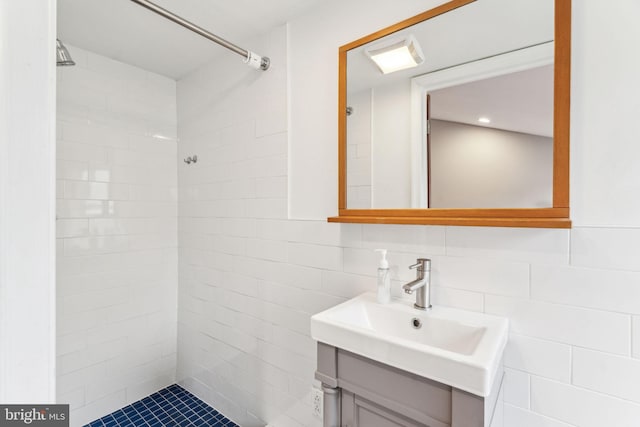 bathroom with tiled shower, vanity, and tile walls