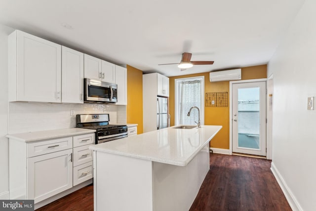 kitchen featuring sink, appliances with stainless steel finishes, a wall mounted AC, an island with sink, and white cabinets