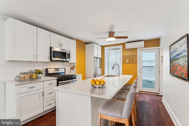 kitchen featuring sink, white cabinetry, a wall mounted AC, an island with sink, and stainless steel appliances