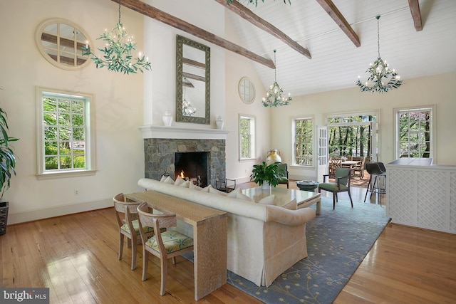 living room featuring an inviting chandelier, beam ceiling, a stone fireplace, and hardwood / wood-style flooring