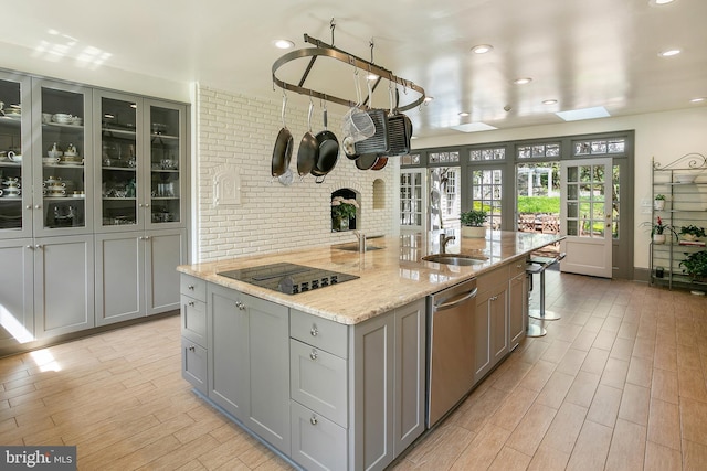 kitchen featuring gray cabinets, dishwasher, an island with sink, light stone countertops, and black electric cooktop