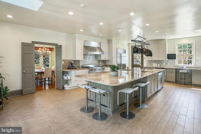 kitchen featuring stainless steel appliances, a spacious island, light stone counters, a kitchen bar, and wall chimney exhaust hood