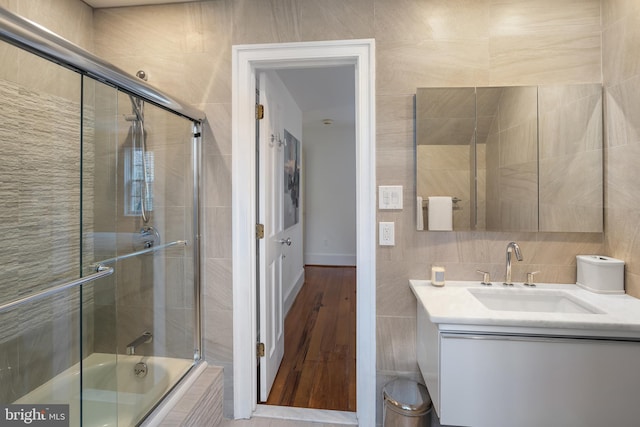 bathroom with enclosed tub / shower combo, vanity, and tile walls