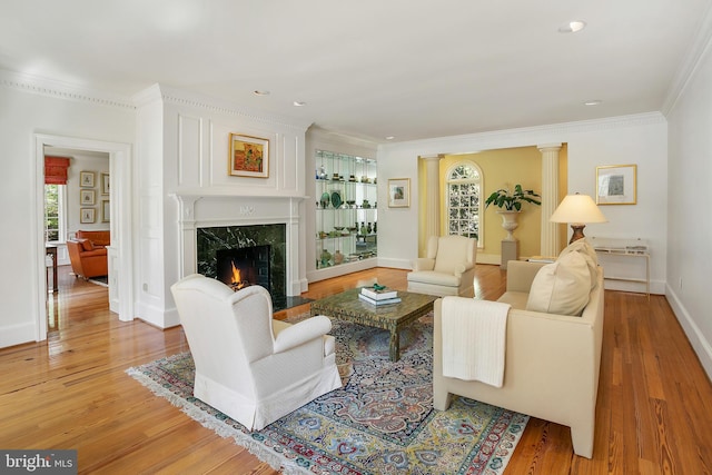 living room featuring crown molding, hardwood / wood-style flooring, a fireplace, and decorative columns