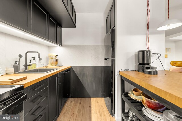 kitchen featuring pendant lighting, light wood finished floors, a sink, wood counters, and dark cabinetry