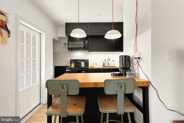 kitchen with butcher block countertops, a sink, a kitchen breakfast bar, black appliances, and decorative light fixtures