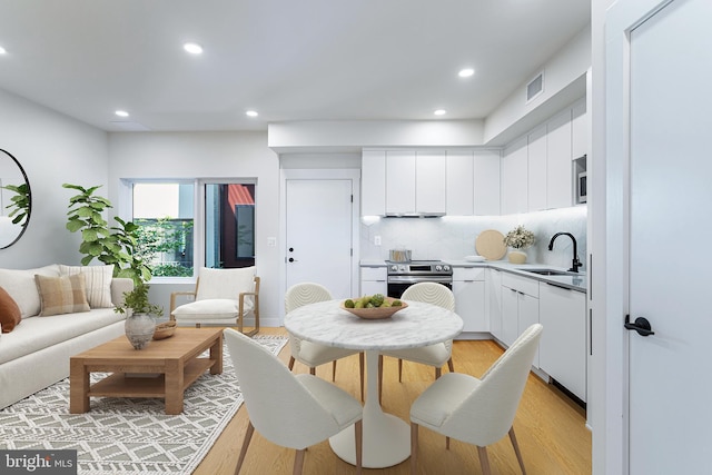 kitchen featuring sink, white cabinetry, light hardwood / wood-style floors, decorative backsplash, and stainless steel range with electric cooktop