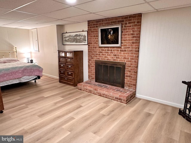 bedroom with a drop ceiling, a fireplace, and light hardwood / wood-style flooring