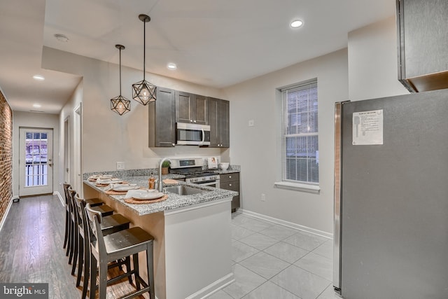 kitchen with pendant lighting, sink, appliances with stainless steel finishes, light stone countertops, and a kitchen bar