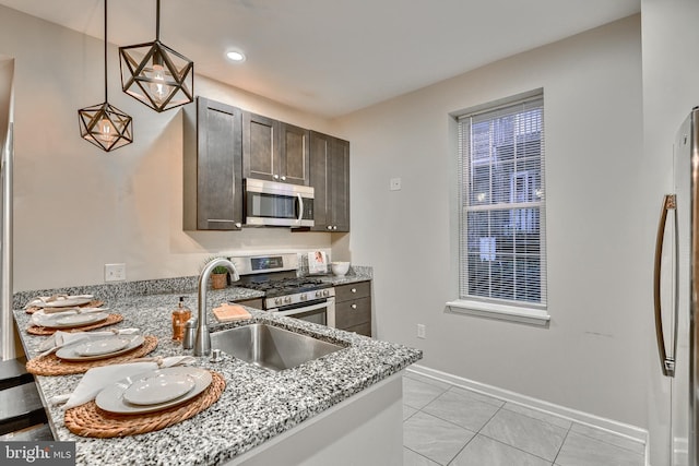 kitchen with sink, appliances with stainless steel finishes, hanging light fixtures, dark brown cabinetry, and light stone countertops