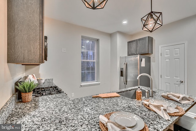 kitchen featuring sink, stainless steel fridge, hanging light fixtures, light stone counters, and kitchen peninsula