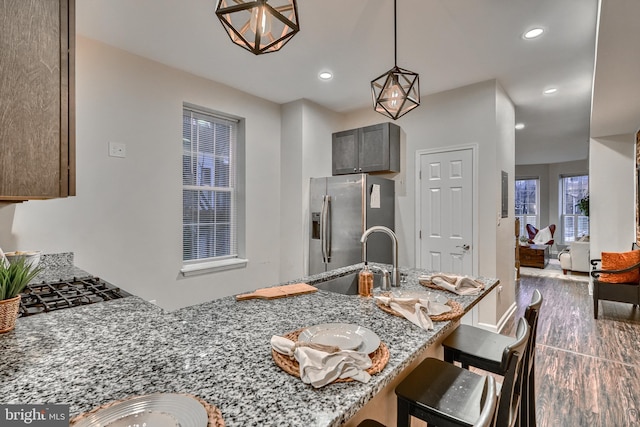 kitchen with light stone counters, a kitchen bar, stainless steel fridge with ice dispenser, decorative light fixtures, and kitchen peninsula