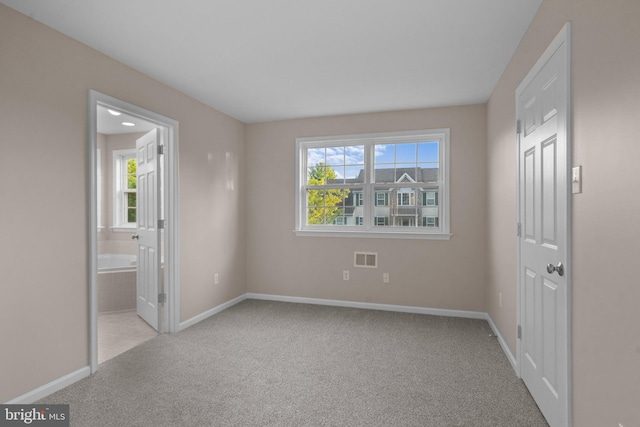 unfurnished bedroom with baseboards, ensuite bathroom, carpet floors, and visible vents