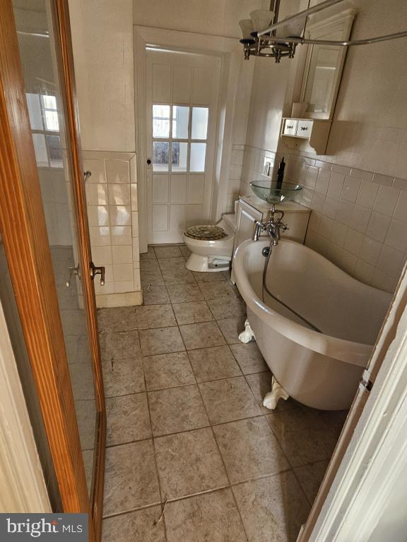 bathroom with tile patterned floors, toilet, a chandelier, tile walls, and a washtub