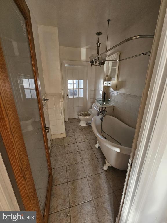 bathroom with tile patterned floors, toilet, tile walls, a bidet, and a bathtub