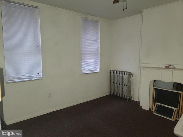 unfurnished living room with ceiling fan, radiator heating unit, and dark colored carpet