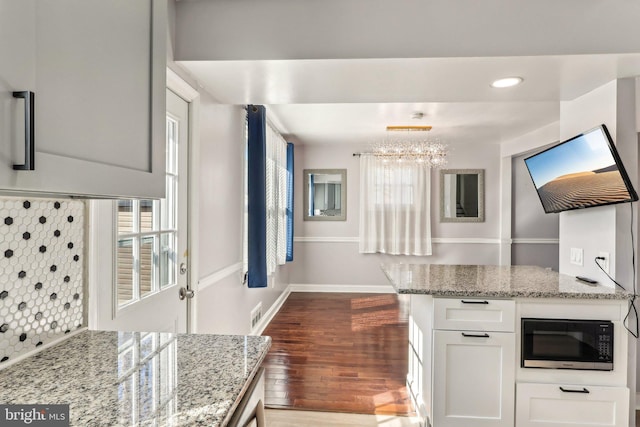 kitchen featuring light stone counters, dark wood finished floors, white cabinetry, black microwave, and baseboards