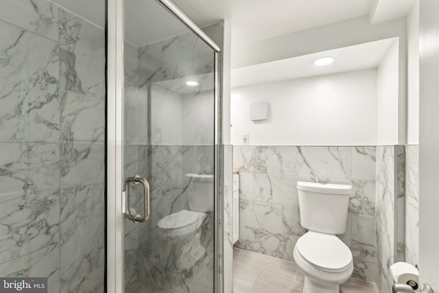 bathroom with toilet, a marble finish shower, and tile walls