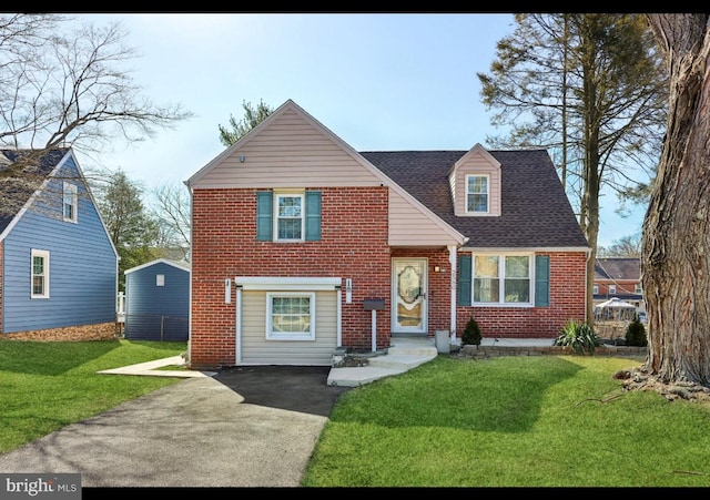 view of front facade featuring brick siding, a front yard, and a shingled roof