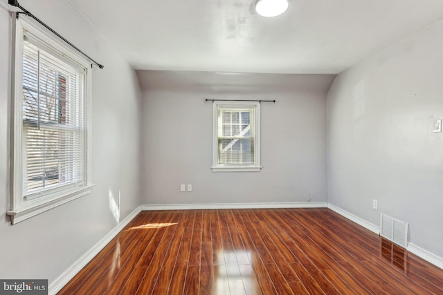 spare room with wood finished floors, visible vents, and baseboards