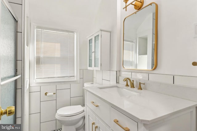 full bathroom featuring a shower with door, tile walls, toilet, and vanity