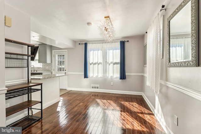 dining area with a chandelier, dark wood-style flooring, visible vents, and baseboards