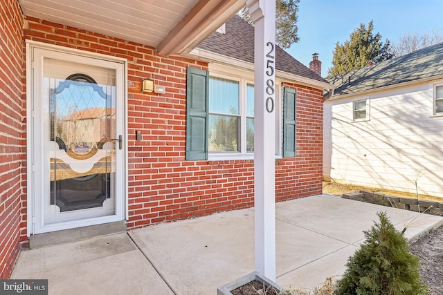 property entrance with a shingled roof and brick siding