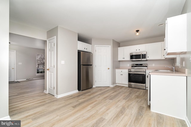 kitchen with light wood finished floors, light countertops, stainless steel appliances, white cabinetry, and a sink