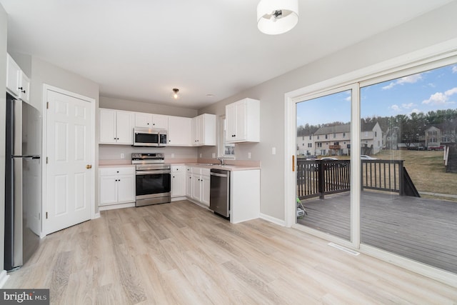 kitchen featuring white cabinetry, light wood-style floors, appliances with stainless steel finishes, light countertops, and baseboards