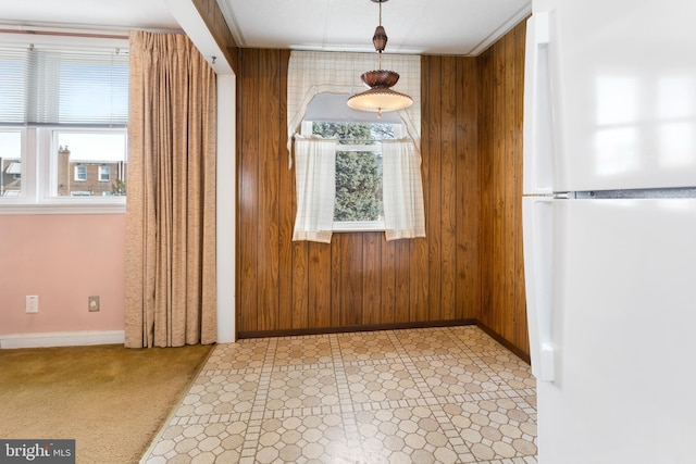 unfurnished dining area featuring light colored carpet, a wealth of natural light, and wood walls