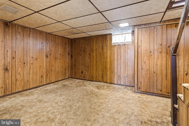 basement featuring a paneled ceiling, light carpet, and wood walls