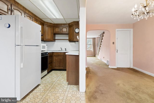 kitchen with pendant lighting, white appliances, a paneled ceiling, light colored carpet, and a chandelier