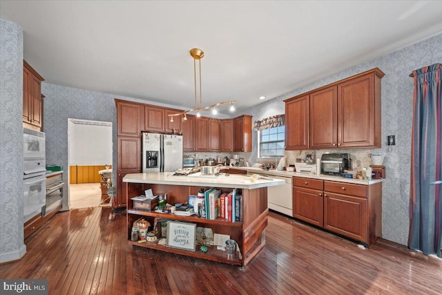 kitchen featuring white appliances, a kitchen island with sink, dark hardwood / wood-style floors, and decorative light fixtures