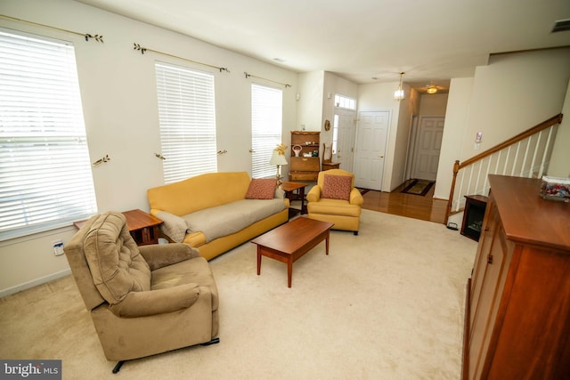 living area with stairs, baseboards, visible vents, and light colored carpet