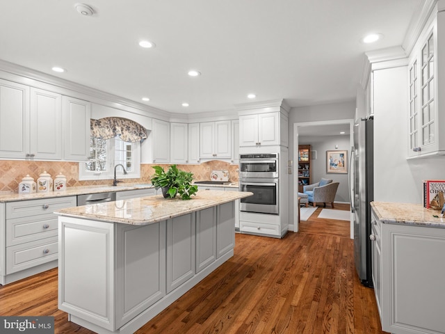 kitchen featuring appliances with stainless steel finishes, white cabinetry, dark hardwood / wood-style flooring, a center island, and light stone countertops