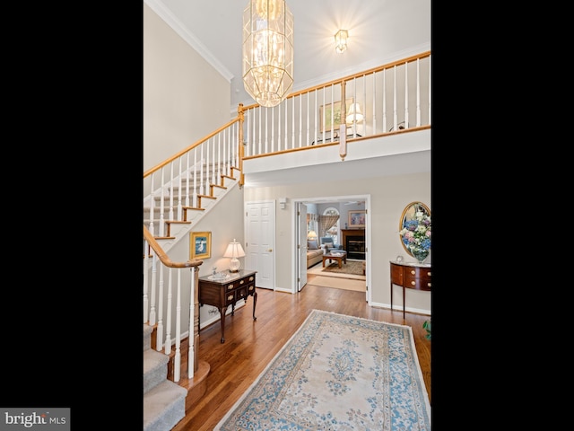 entrance foyer featuring crown molding, a towering ceiling, wood-type flooring, and an inviting chandelier