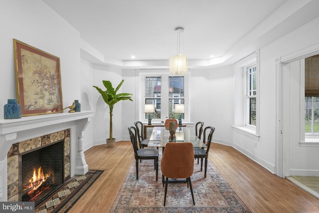 dining space with a tile fireplace, hardwood / wood-style floors, and a tray ceiling