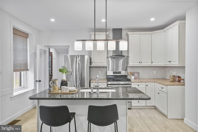 kitchen featuring white cabinetry, an island with sink, appliances with stainless steel finishes, and dark stone counters