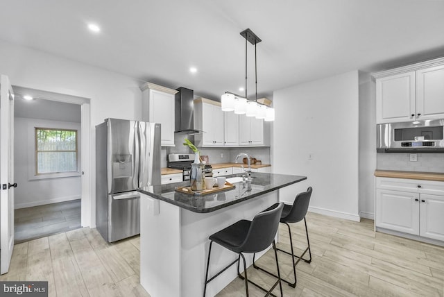 kitchen featuring stainless steel appliances, a center island with sink, wall chimney range hood, and white cabinets