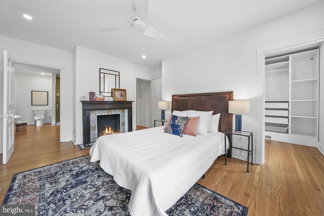 bedroom with hardwood / wood-style flooring, ceiling fan, and a fireplace