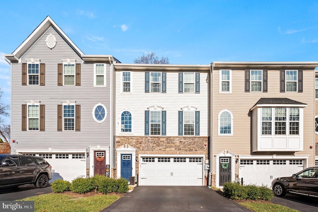 townhome / multi-family property with an attached garage, driveway, and stone siding