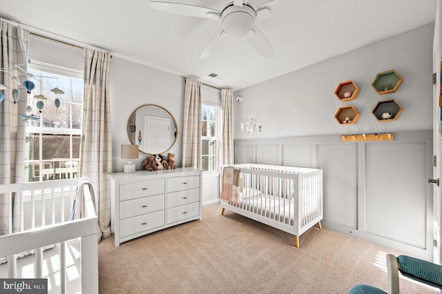 bedroom with visible vents, a decorative wall, a nursery area, and light carpet