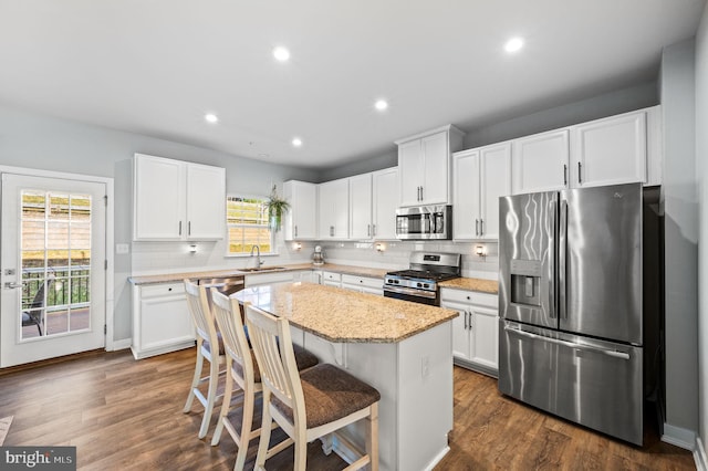 kitchen featuring tasteful backsplash, a center island, stainless steel appliances, white cabinetry, and dark wood-type flooring