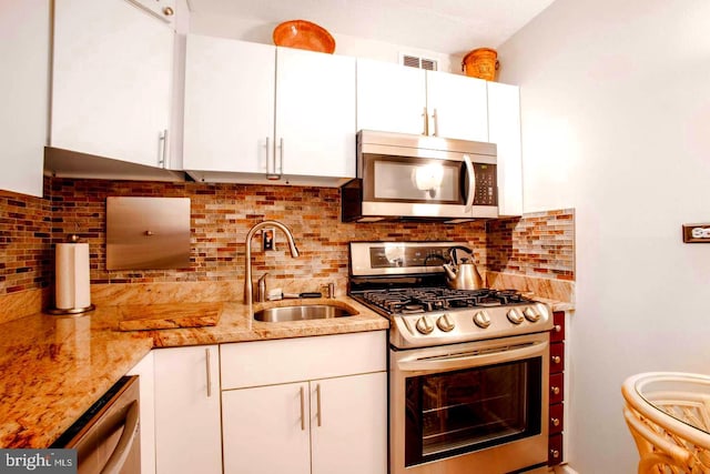 kitchen featuring appliances with stainless steel finishes, a sink, white cabinetry, and light stone countertops