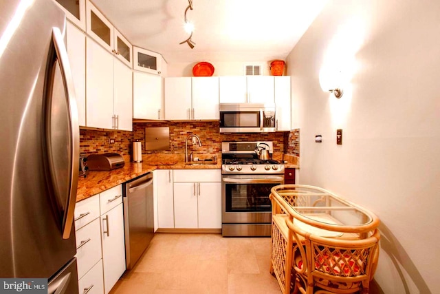 kitchen featuring tasteful backsplash, appliances with stainless steel finishes, glass insert cabinets, white cabinets, and a sink