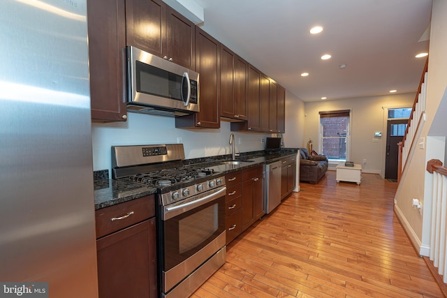 kitchen featuring light hardwood / wood-style flooring, stainless steel appliances, dark brown cabinetry, sink, and dark stone countertops