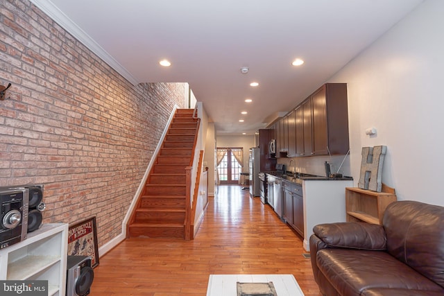 living room featuring french doors, light hardwood / wood-style flooring, brick wall, sink, and ornamental molding
